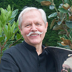 A man with a white mustache wearing a black shirt holding an instrument.