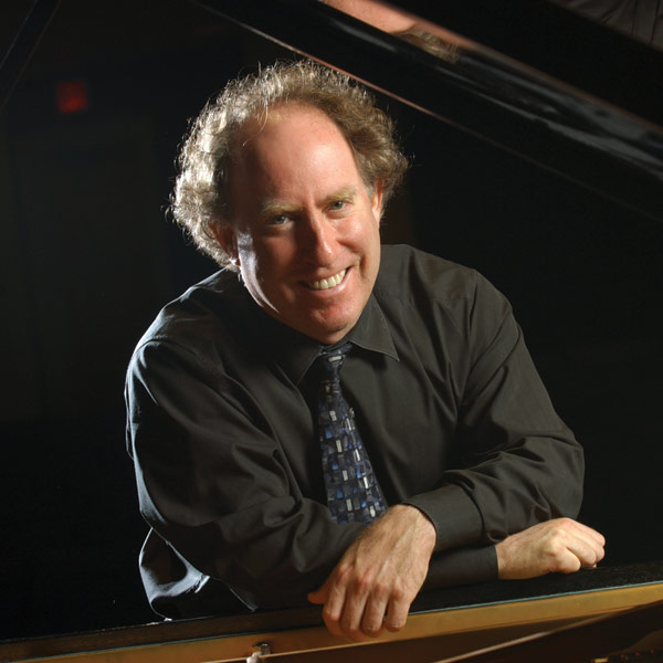 Jeffrey Kahane leaning against piano.