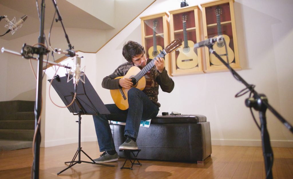 A classical guitarist recording in a studio.
