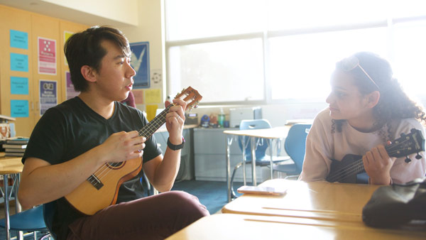 Thornton Community Engagement mentor Jim Wang demonstrates a ukulele technique to a student in a classroom. 