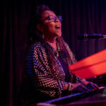 Image of a woman singing and playing at the piano.