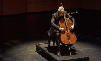 Photo of cellist on stage under spotlight