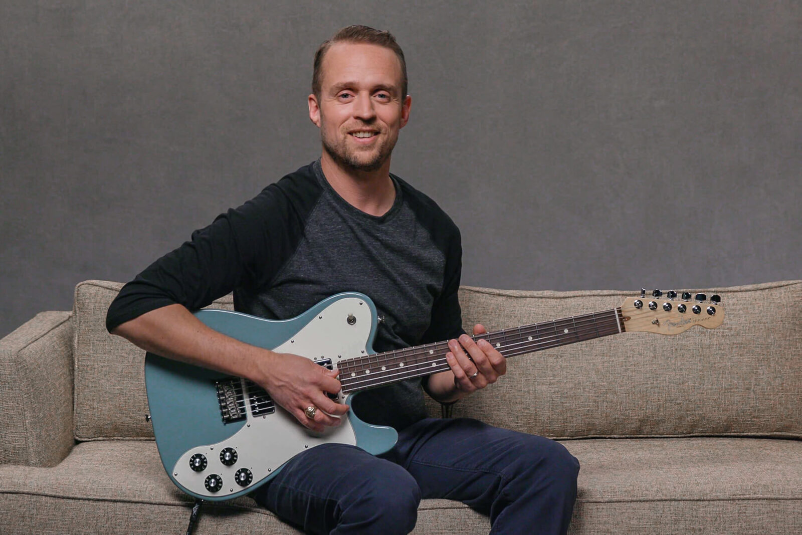 Matt Lake pictured on sofa with guitar 