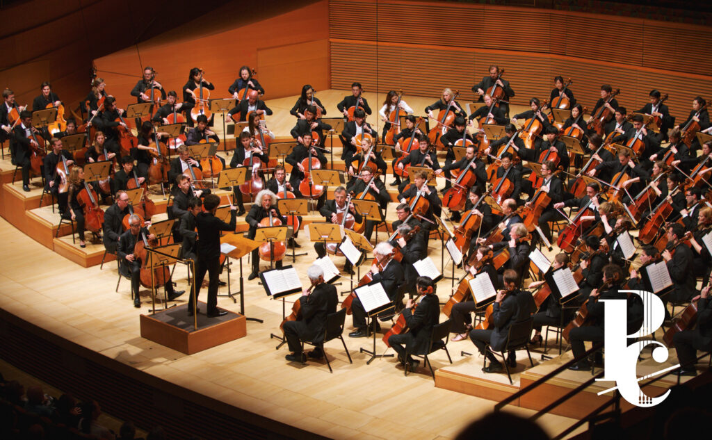 Photo of mass cello ensemble in Disney Hall with white logo