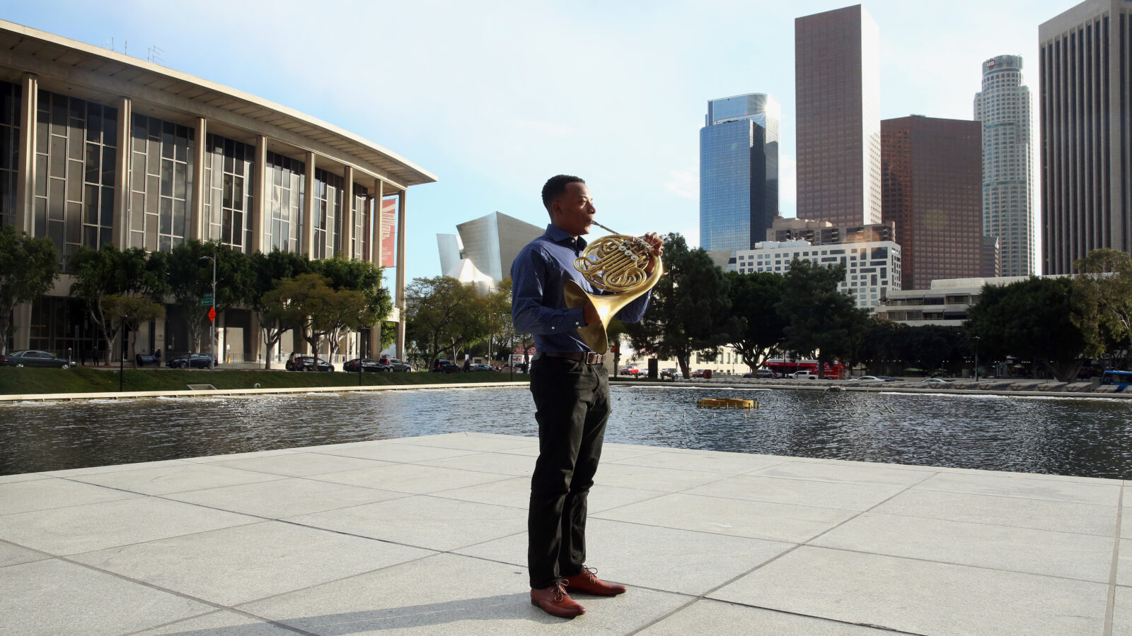 Malik Taylor stands in downtown LA holding french horn 