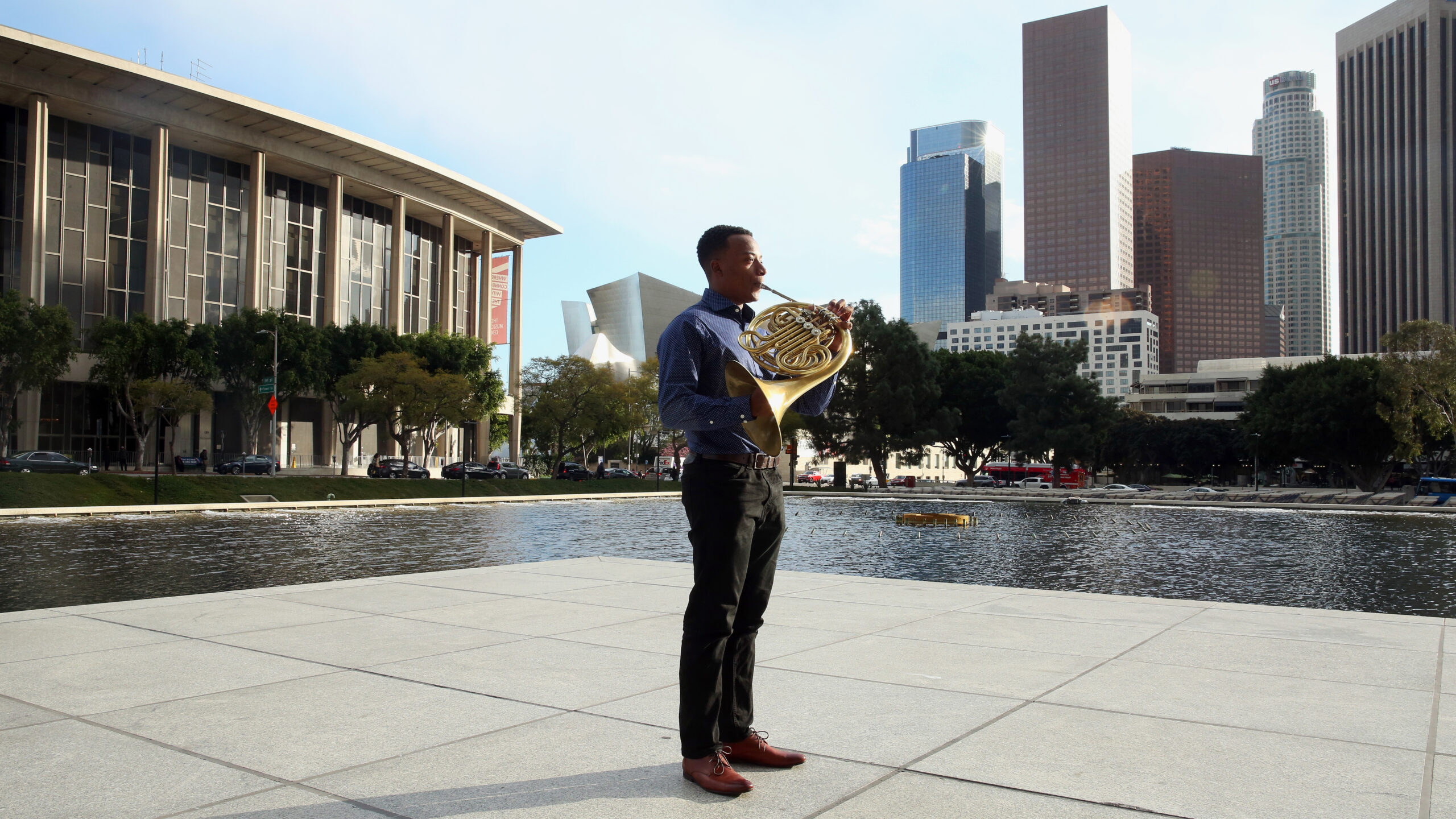 Man stands in downtown LA holding french horn