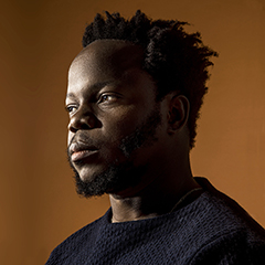 Ambrose Akinmusire in dark sweater with orange backdrop