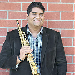 Andrew Harrison holding saxophone on brick background