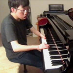 Wayne Yang sits at piano with hands on keys