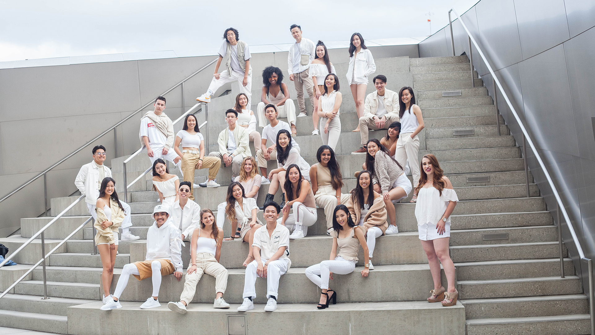 A group of dancers dressed in white standing on a sloping set of concrete stairs