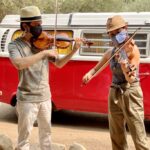 Photo of two violinists playing outdoors while wearing masks over their faces
