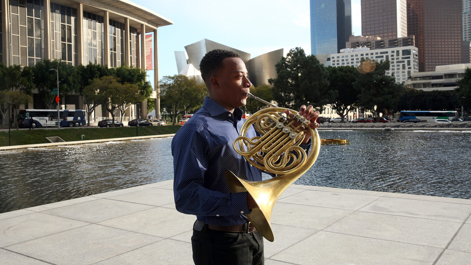 Malik Taylor stands in downtown LA holding french horn 