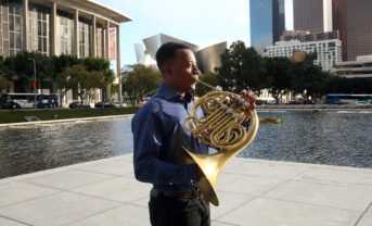 Malik Taylor stands in downtown LA holding french horn