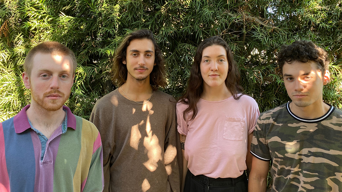 Four musicians of Avellana group standing side by side in front of greenery