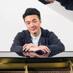 Barry Tan with arms on a piano, looking into the camera