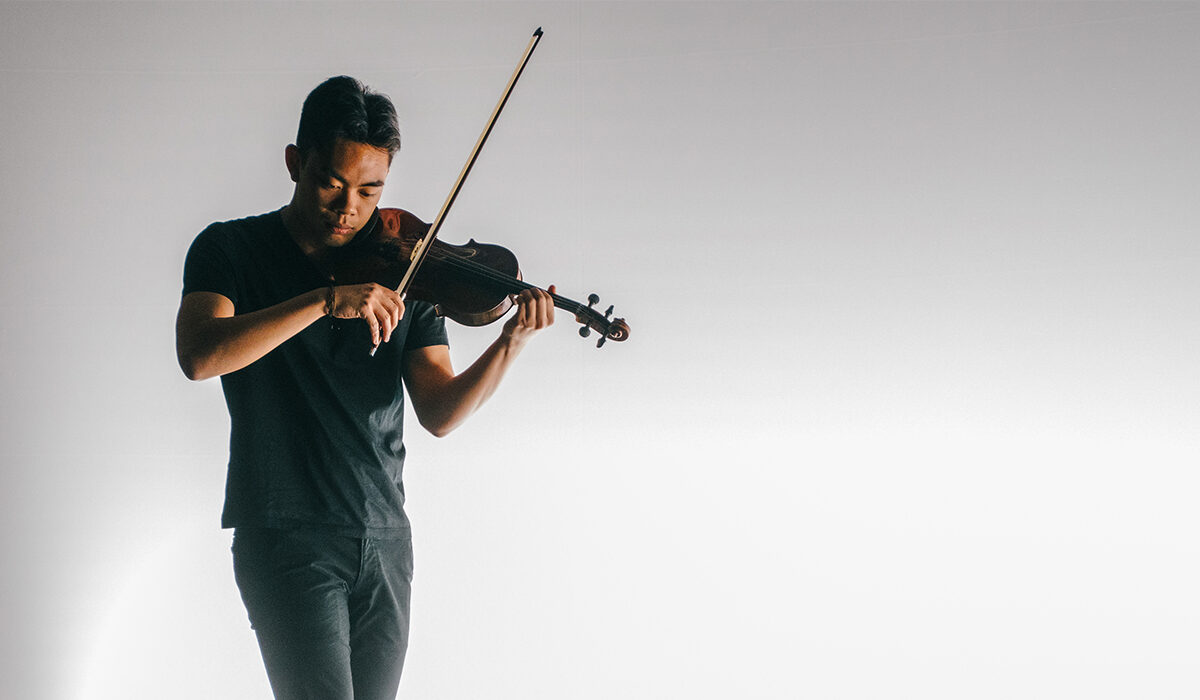 Violinist dressed in black, performing on a sharply lit stage
