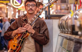 Image of student holding an electric guitar with neon signs in the background.
