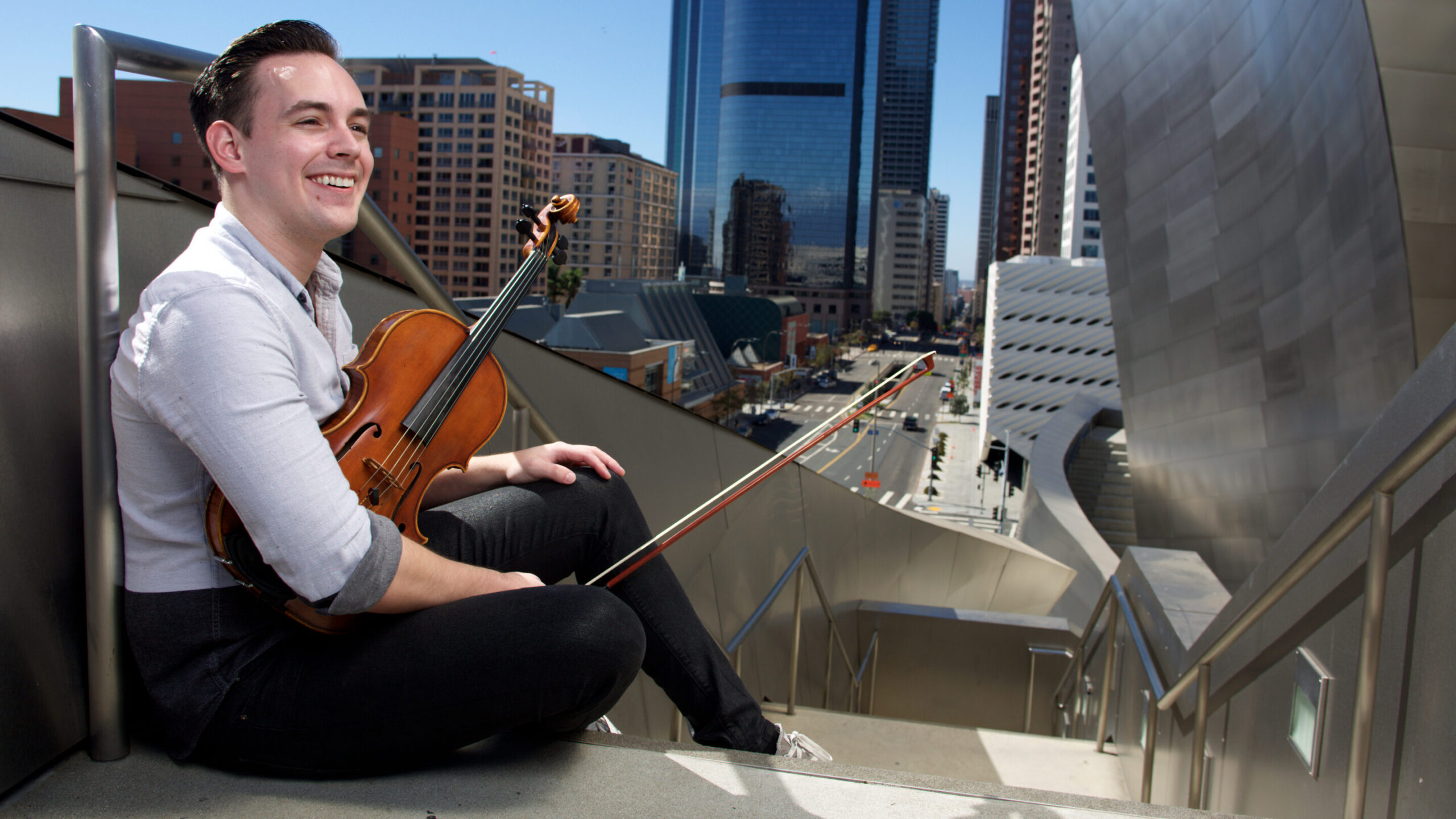 Student violinist holding their instrument smiles outside Walt Disney Concert Hall in Downtown Los Angeles.  