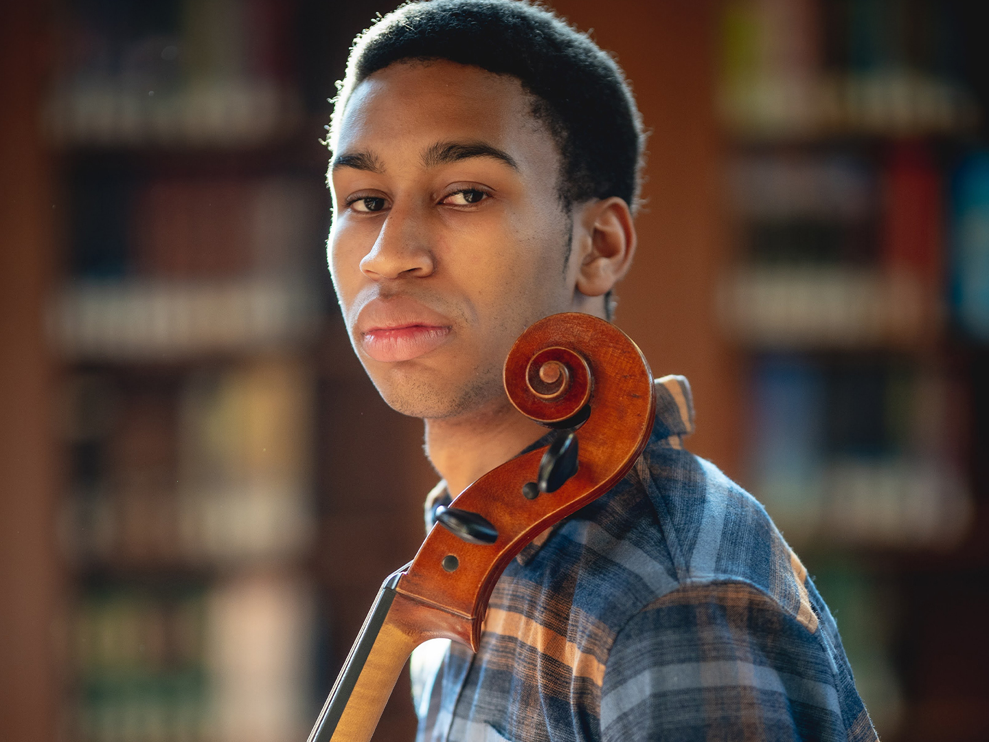 Photo of composer and cellist Quenton Blache standing in sunlight through a window in a library. 