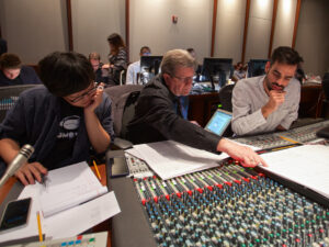 Daniel Carlin mentors two students to his left and right in front of an audio mixing console at Warner Bros. Eastwood Scoring Stage. 