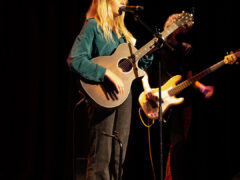 Photo of singer with an acoustic guitar performing on stage