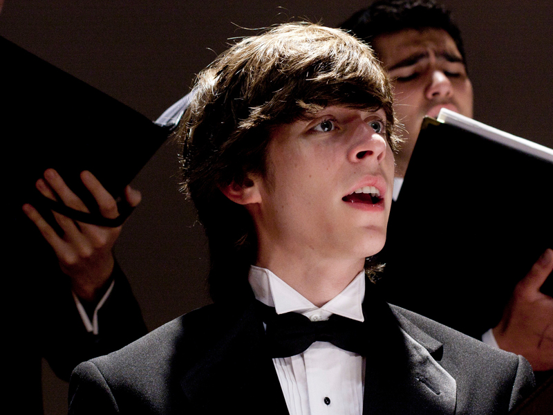 A USC Thornton student in concert attire sings onstage with the rest of the ensemble. 