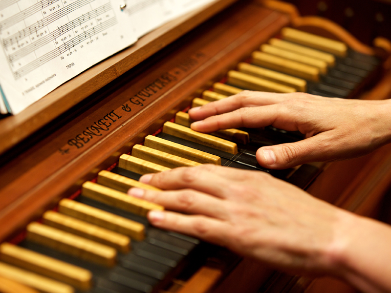This picture shows the hands of a member playing on a harpsichord while looking at the score.  