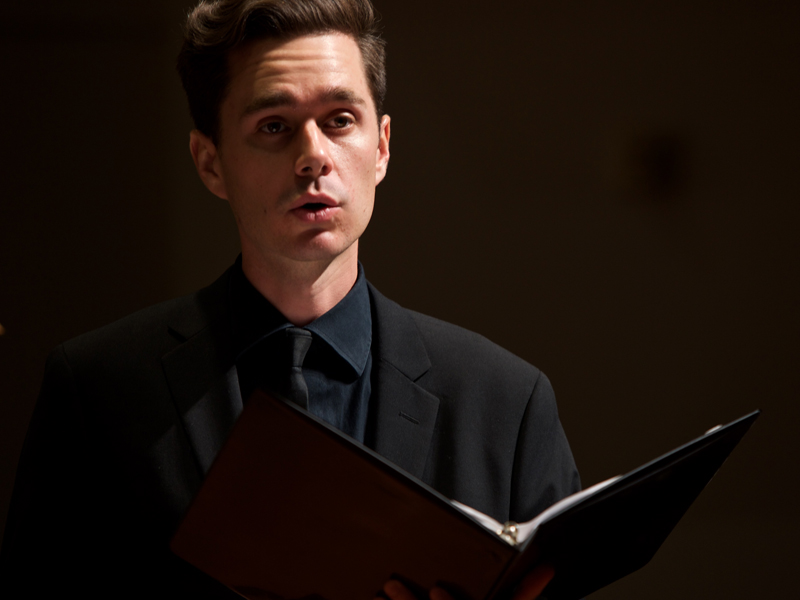 A USC Thornton student in black concert attire sings onstage with a book of libretto on his left hand. 