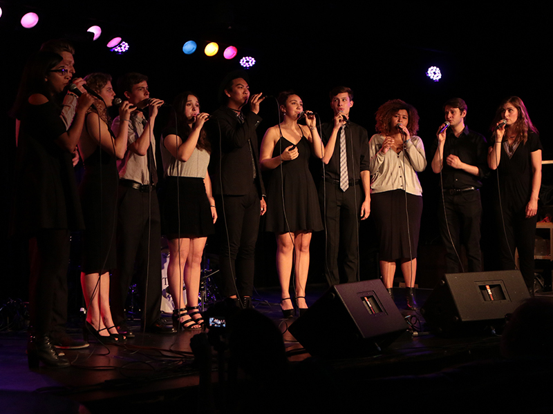 The vocal jazz ensemble sings onstage. They are in various concert attire. 