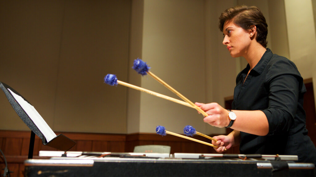 A student plays percussion onstage indoors at the Newman Recital Hall. 