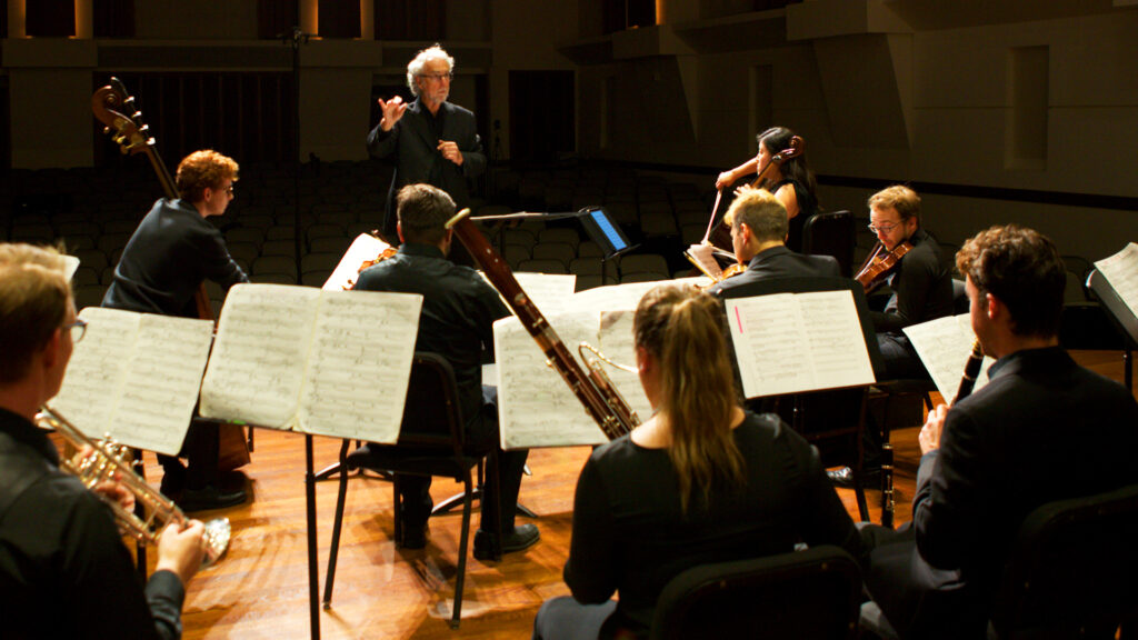 Composition chair Donald Crockett conducts a group of students onstage indoors. 
