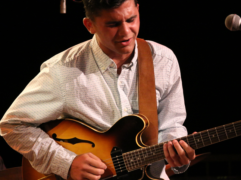 A USC Thornton jazz student in white concert attire plays the electric guitar. 