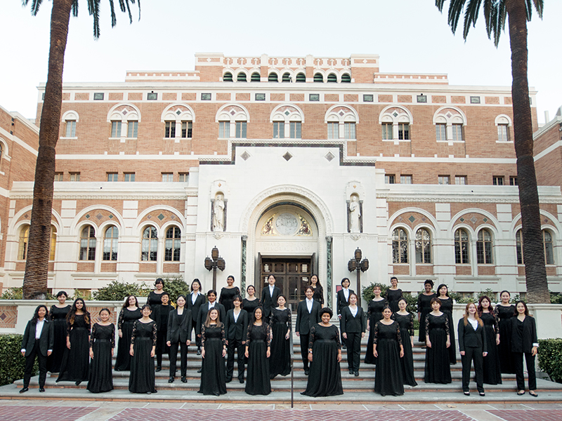 The entire choir stands on the front steps of the Dohenyi Memorial Library at USC for this picture. They are dressed in black concert attire. 