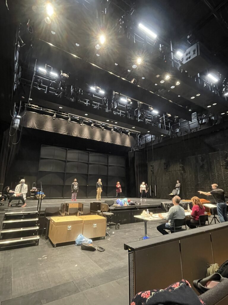 Second of three pictures showing a rehearsal taking place onstage indoors