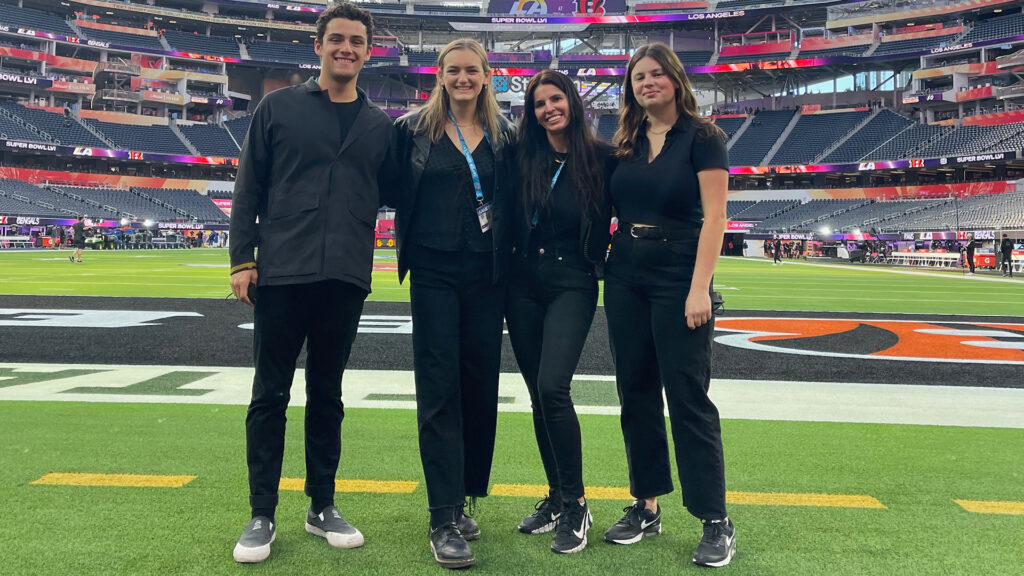 Three students and USC Thornton faculty member Sophie Reeves stand at the end zone of the football field at SoFi Stadium in Los Angeles. 