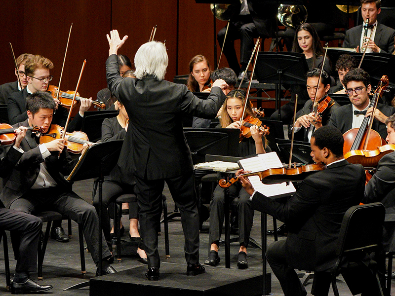 Artistic Leader Carl St. Clair raises his left hand and tilts his right hand in this picture with conducting the Thornton Symphony onstage. 