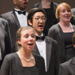 This picture zooms on 3 of the Golden Bridge members singing onstage.