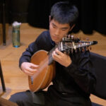 Photo of student lutenist playing on stage with an early music ensemble.