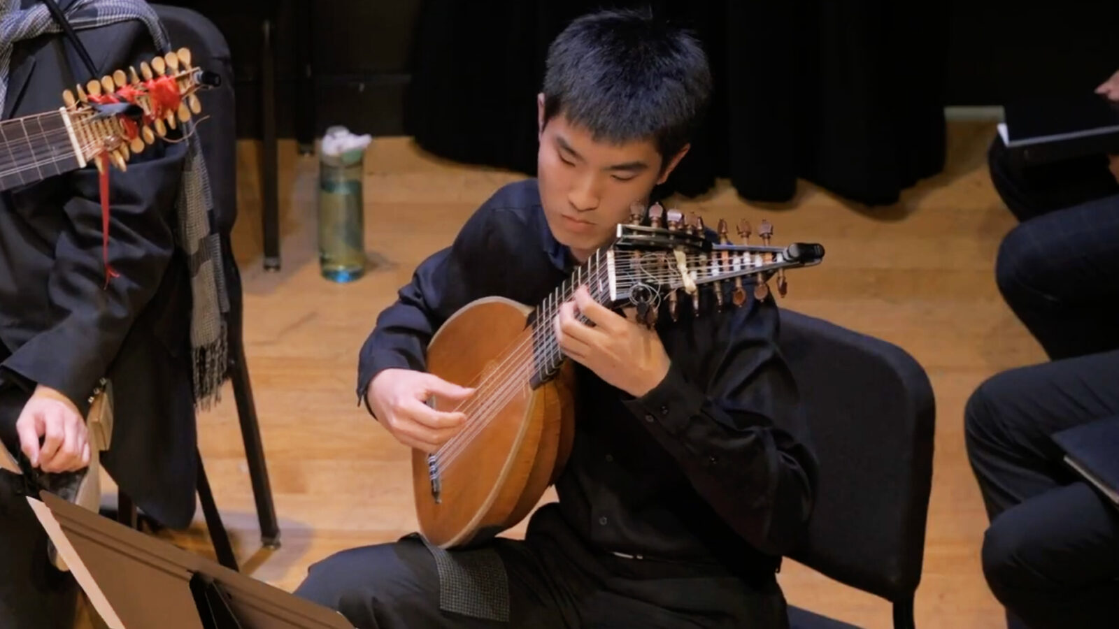 Photo of student lutenist playing on stage with an early music ensemble. 