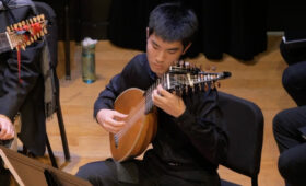 Photo of student lutenist playing on stage with an early music ensemble.