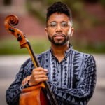 Cellist Seth Parker Woods standing with their cello instrument.