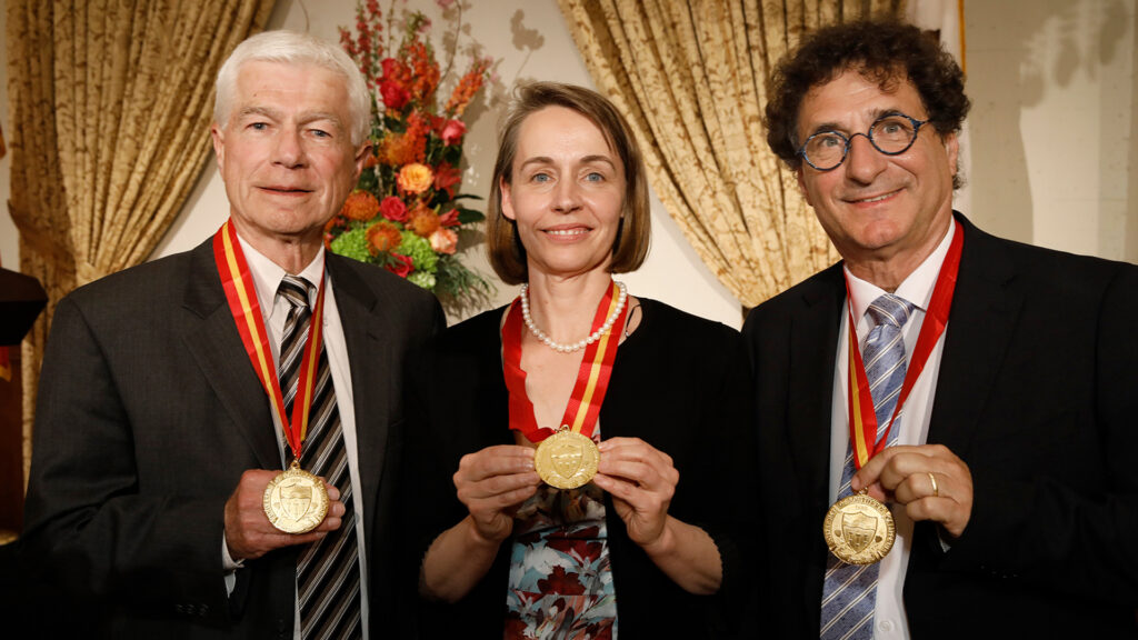 Robert Cutietta stands with honorees Daniel Mazmanian and Sarah Van Orman with gold medallions.