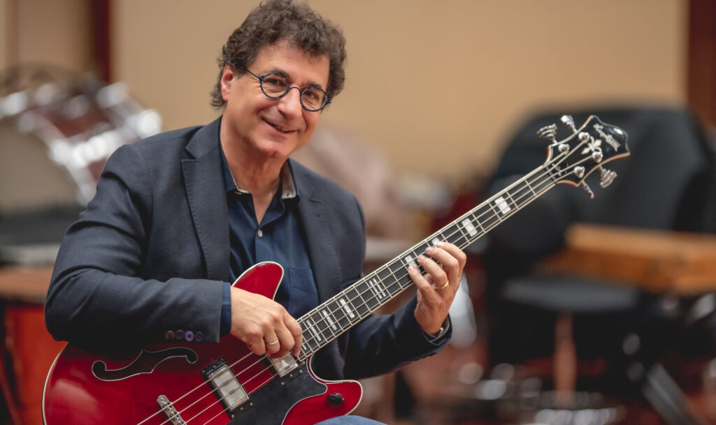 Robert Cutietta playing a red bass guitar indoors.