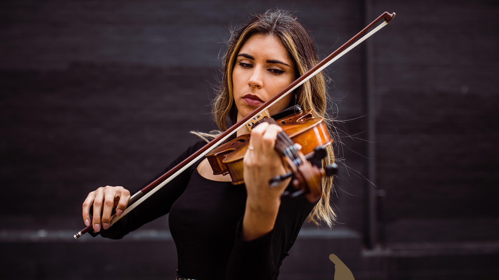 Photo of a musician with long hair in concert attire playing the viola. 