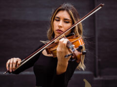 Photo of a musician with long hair in concert attire playing the viola.