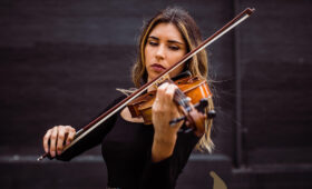 Photo of a musician with long hair in concert attire playing the viola.