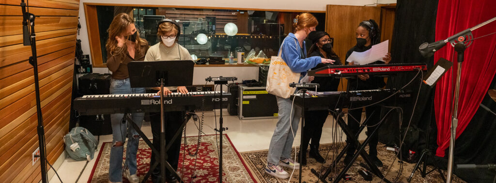 Indoor photo of popular music students learning how to use recording equipment in a professional sound studio.