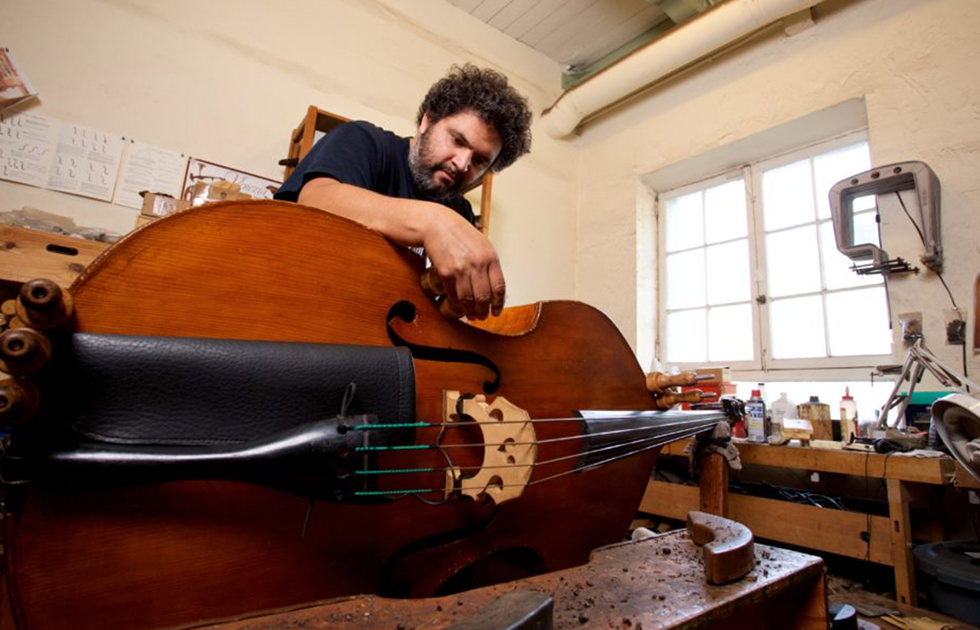 Photo of someone repairing a double bass indoors.