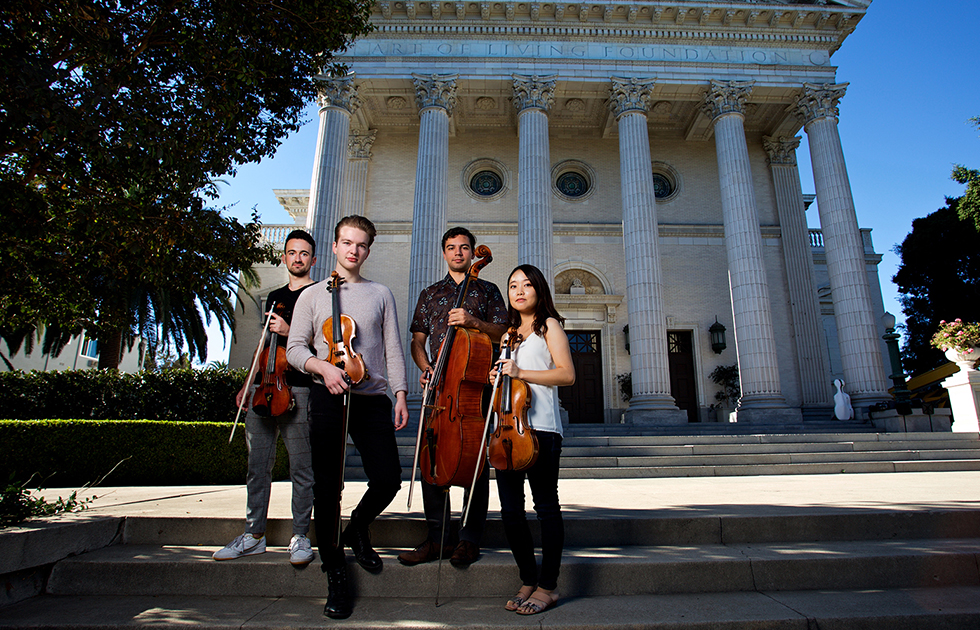 A string quartet with their instruments, stand outside a historic building.