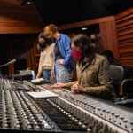 Photo of popular music students working around a professional mixing board at a sound studio.